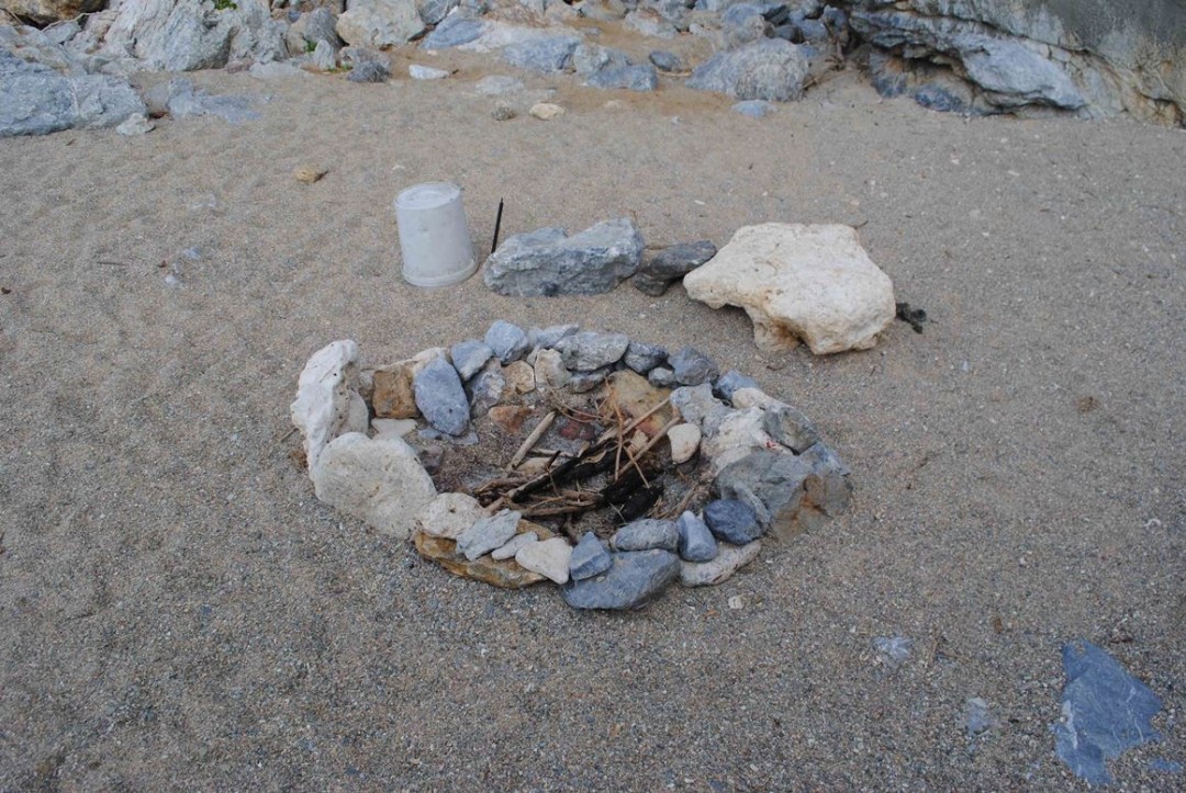 写真２　炉あと１（現代）　炉辺に置石（腰掛け）とバケツ、 火かき棒がある。炉内には燃え残った薪がある